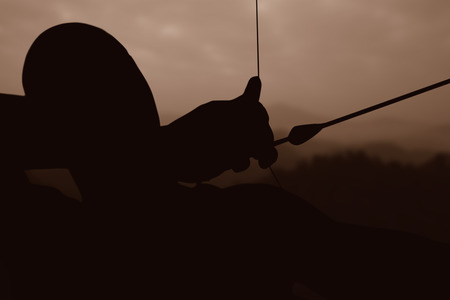 Close up of man stretching his bow against trees and mountain range against cloudscapeの写真素材