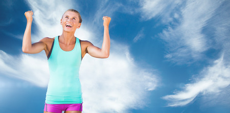 Athletic woman with arms up against blue sky with clouds
