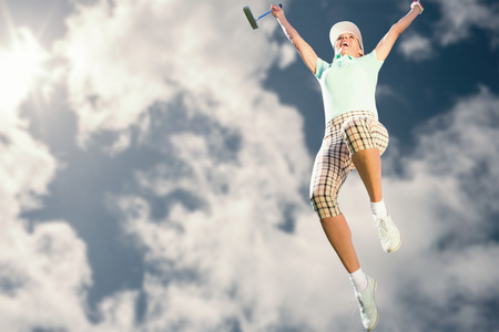 Woman jumping with golf club against bright blue sky with cloudsの写真素材