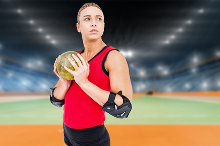 Female athlete with elbow pad holding handball against handball field indoorの写真素材
