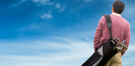 Man carrying golf equipment against blue skyの写真素材