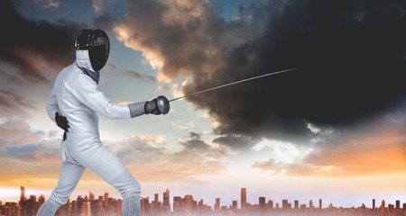 Man wearing fencing suit practicing with sword against city on the horizonの写真素材