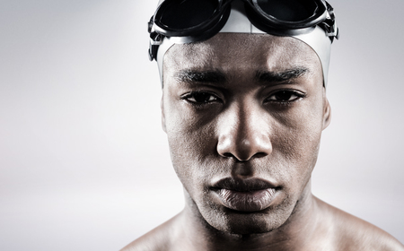 Portrait of swimmer in swimmingÂ goggles and swimming cap against grey backgroundの写真素材