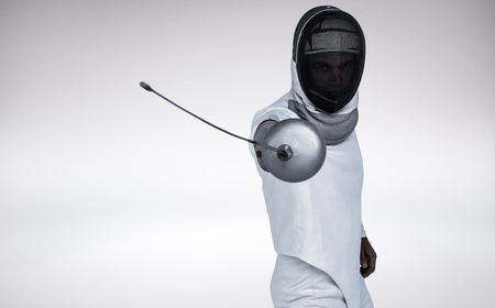 Man wearing fencing suit practicing with sword against grey background