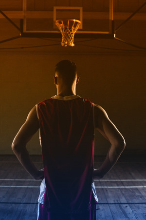 Basketball player with his hands on his hips looking the basketball hoopの写真素材
