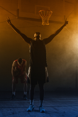 Victorious basketball player raising his arms up while his rival looking downの写真素材