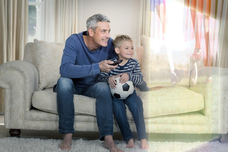 Composite image of father and son are watching sport match on television at homeの写真素材