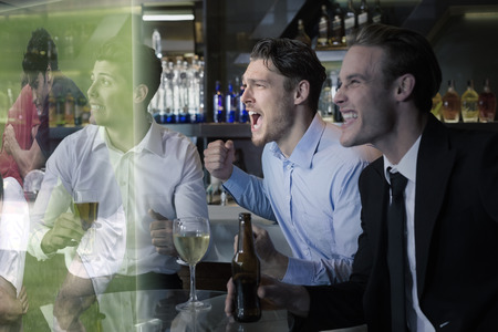 Handsome friends having a drink together against rugby players tackling during gameの写真素材
