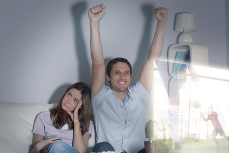 Composite image of man is watching sport on television next to his bored wife at homeの写真素材