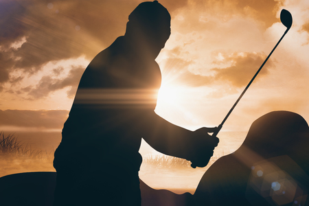 Golf player taking a shot against sunrise over grassの写真素材
