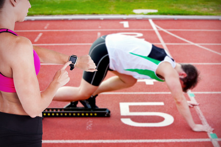 Female athlete using her smart watch against athletic man on the starting line putting his foot in...
