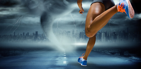 Sporty woman finishing her run against stormy sky with tornado over roadの写真素材