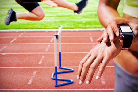 Close up on a sportswoman wearing a connected watch  against assertive male athlete jumping above hedge during a raceの写真素材