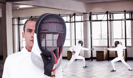 Swordsman holding fencing mask against interior view of a gym