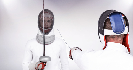 Man wearing fencing suit practicing with sword against grey background