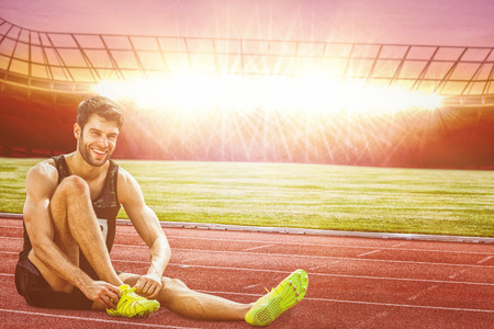 Sportsman smiling and lacing shoes  against race track