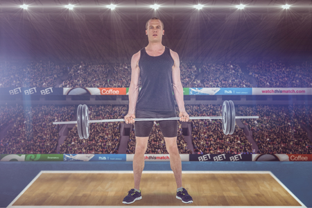 Bodybuilder lifting heavy barbell weights against view of a stadiumの写真素材