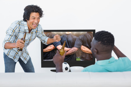Soccer fans watching tv against rugby players standing together before matchの写真素材