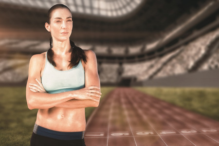 Sporty woman posing with her arms crossed against view of a running trackの写真素材