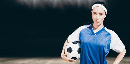 Woman football player posing with football on a white backgorund against football pitch at night with lightsの写真素材
