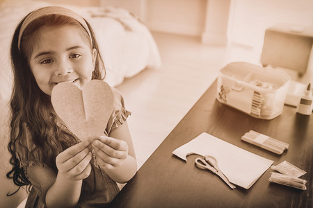 High angle portrait of a cute young girl holding heartshape paper at tableの写真素材