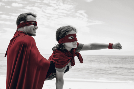 Close-up of happy father and son in superhero costume enjoying at beachの写真素材