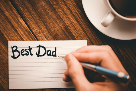 happy fathers day against human hand writing on paper at desk with coffee cupの写真素材