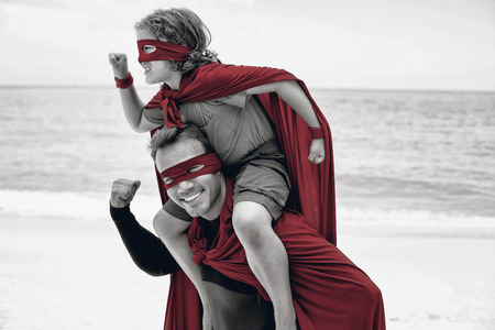 Happy father and son in superhero costume pretending to run at beachの写真素材