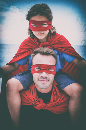 Portrait of confident father in superhero costume carrying son on shoulder at beachの写真素材