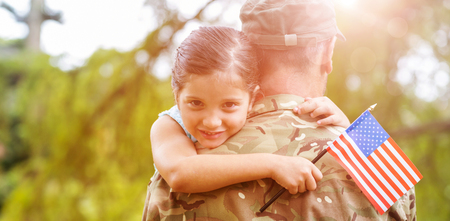 Portrait of smiling girl holding american flag while hugging army officer father in parkの写真素材