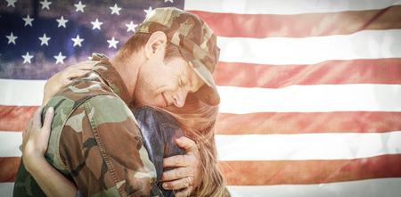 American soldier embracing his partner in front of american flag while reunitingの写真素材