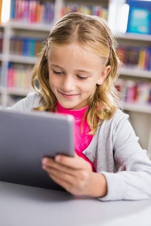 Schoolgirl using digital tablet in library at schoolの写真素材