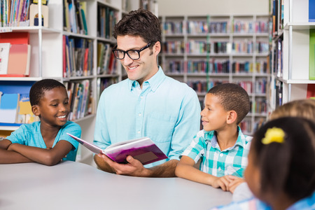Teacher and kids reading book in library at school