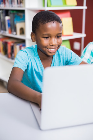 Schoolboy using laptop in library at school