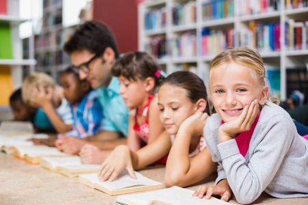 Teacher and kids lying on floor reading book in library
