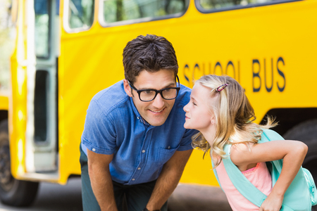 Smiling schoolgirl about to kiss a teacher in front of school bus