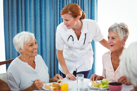 Smiling nurse looking at senior person during breakfast in a retirement homeの写真素材