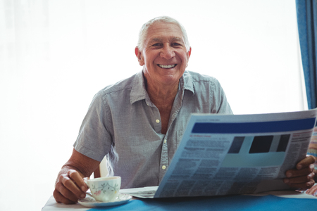 Retired smiling man looking at the camera while holding newspaperの写真素材
