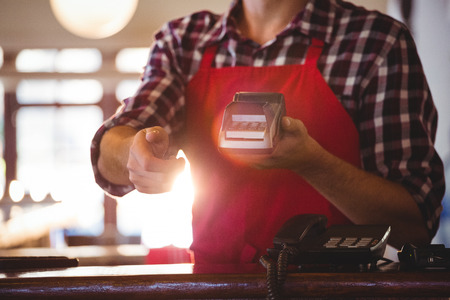 Mid section of waiter showing credit card machine at cafÃ©