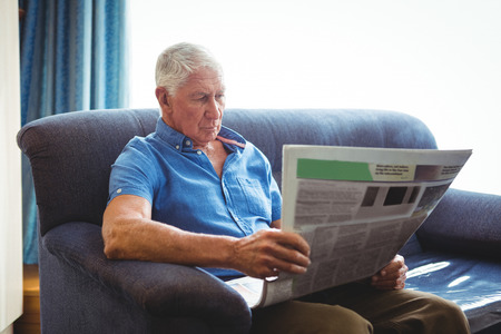 Senior man seated on a sofa reading newspaperの写真素材