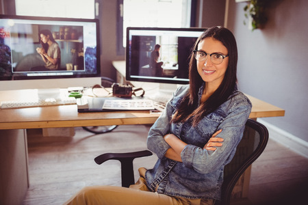 Portrait of happy female graphic designer sitting with arms crossed at officeの写真素材