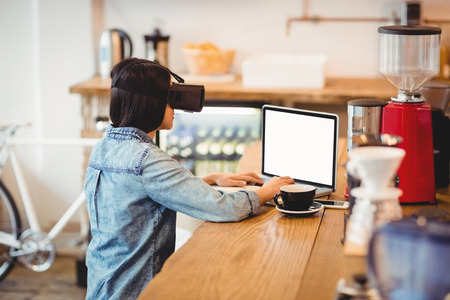 Young woman using the virtual reality headset while working on laptop