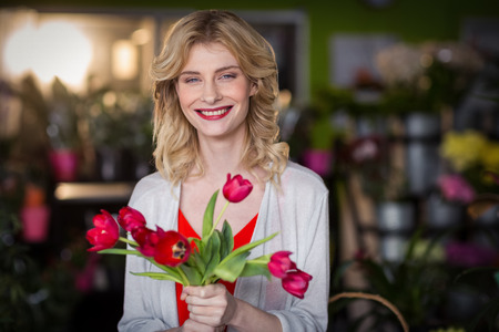 Portrait of happy female florist holding bunch of flower in the shopの写真素材