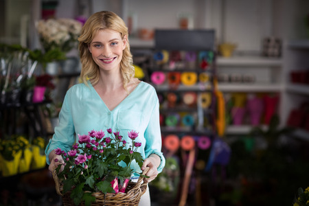 Portrait of happy female florist holding basket of flowers in the shopの写真素材