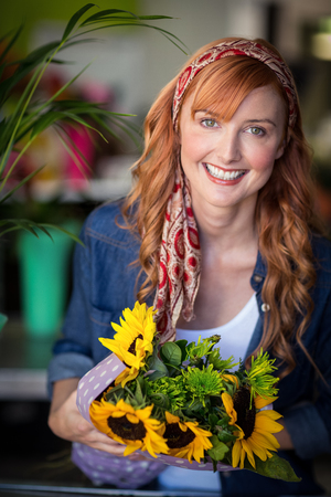 Portrait of smiling female florist holding bunch of flower in flower shopの写真素材