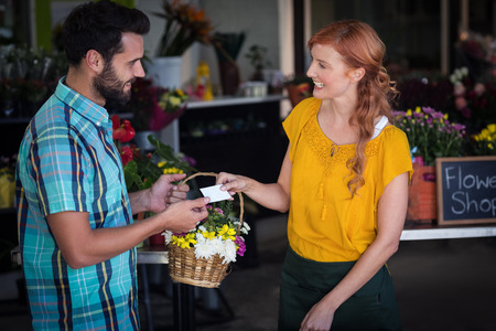 Female florist giving visiting card and flower basket to customer in the flower shopの写真素材