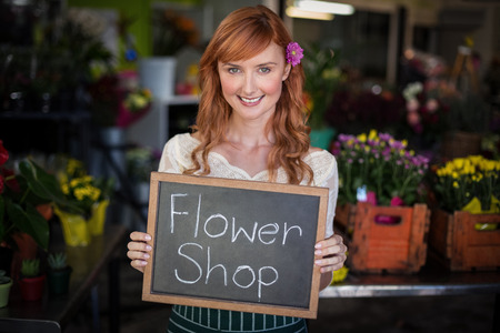 Portrait of female florist holding slate with flower shop sign in the flower shopの写真素材