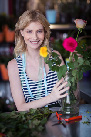 Portrait of smiling female florist arranging flower bouquet in vase at flower shopの写真素材