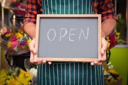 Mid section of male florist holding open sign on slate at his flower shop