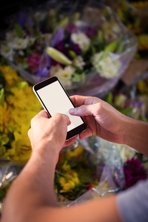 Male florist text messaging on mobile phone at his flower shopの写真素材